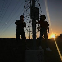 two people standing on top of a power pole at sunset